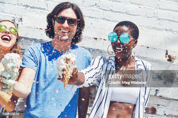 young man and women holding melting ice cream cones, showering in sugar strands - ice cream sprinkles stock pictures, royalty-free photos & images
