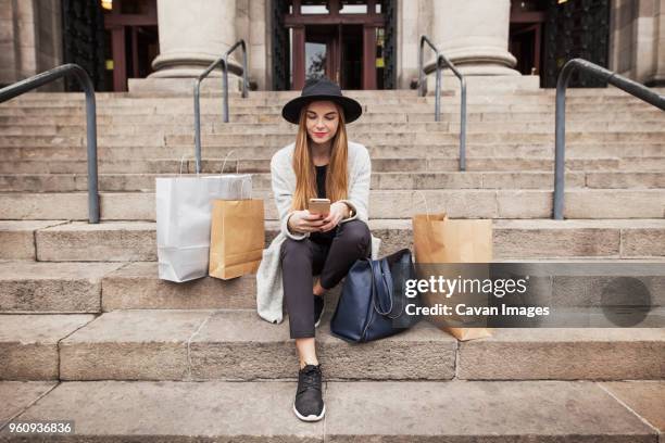 woman text messaging while sitting by shopping bags on steps - young women shopping stock pictures, royalty-free photos & images