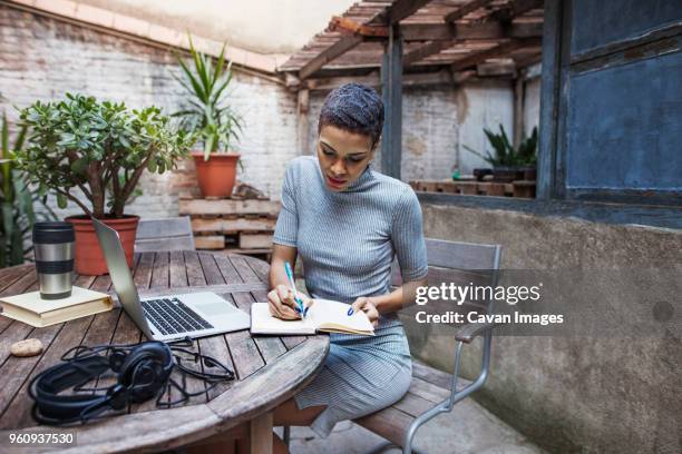 serious businesswoman writing in book at table - african creative with laptop working outside stock-fotos und bilder