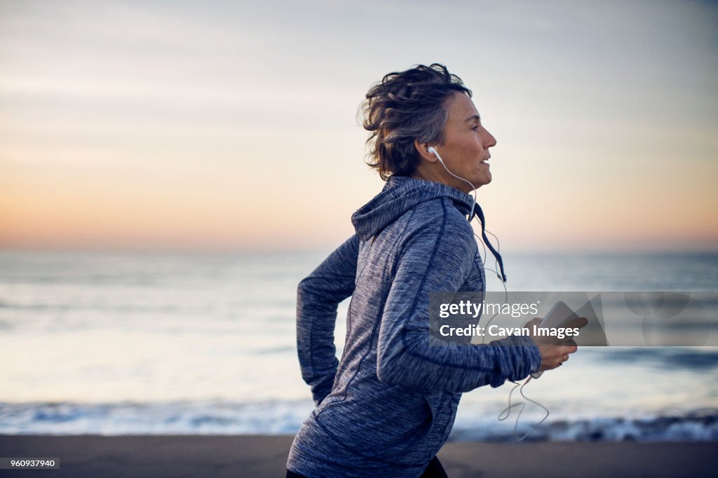 Woman jogging while listening music at beach against sky