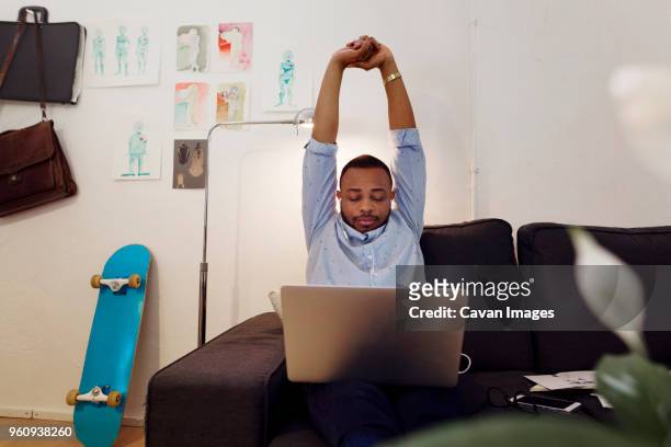 Tired businessman stretching hands while working on laptop in creative office