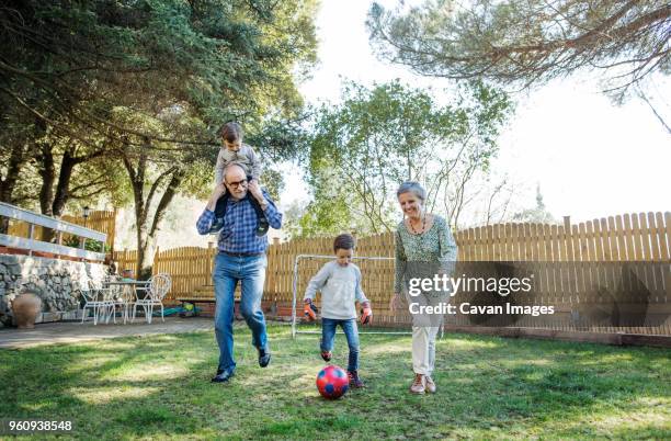 full length of grandparents and grandsons playing soccer at yard - fences 2016 film stock-fotos und bilder