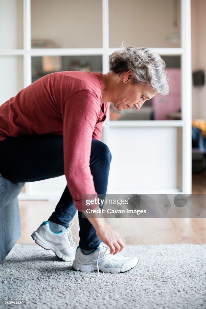 Side view of mature woman tying shoelace at home