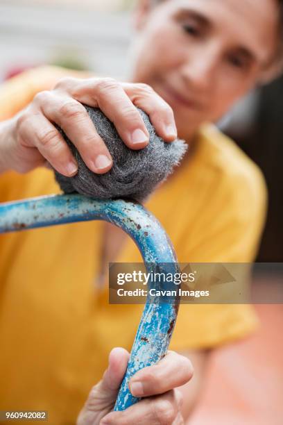 close-up of mature woman scrubbing metallic chair with steel wool at yard - brillos stockfoto's en -beelden