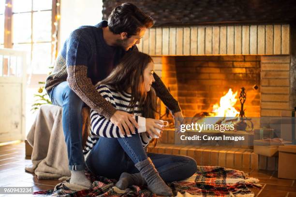 couple with coffee cup looking at fireplace while sitting on floor - foyer de cheminée photos et images de collection