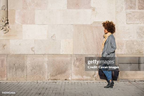 side view of woman carrying bag while walking on footpath by wall - woman side view walking stock pictures, royalty-free photos & images