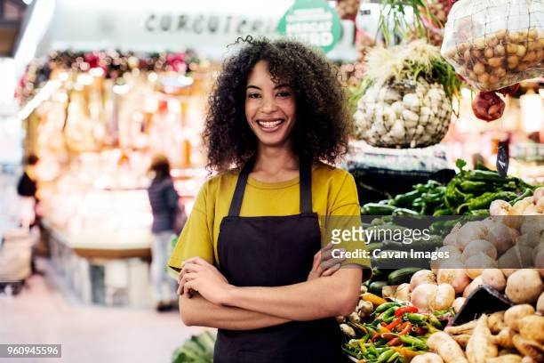 portrait of confident owner with arms crossed standing at market stall - apron lady stock-fotos und bilder