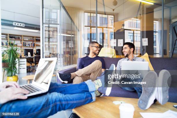 low section of businessman using laptop computer while coworkers smiling in office - lower employee engagement stock pictures, royalty-free photos & images