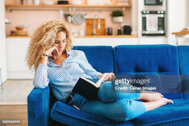 full length of woman reading diary while reclining on sofa at home - book blue bildbanksfoton och bilder