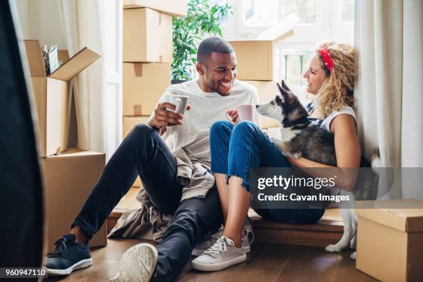 happy couple playing with dog while sitting at doorway in new house - verhuizen stockfoto's en -beelden