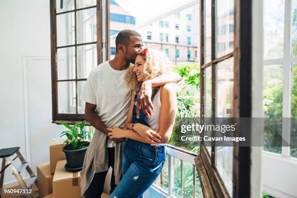 husband kissing wife on forehead while standing by window in new house - new husband stock pictures, royalty-free photos & images