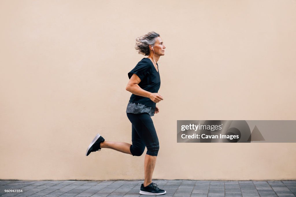 Side view of woman jogging on footpath against wall