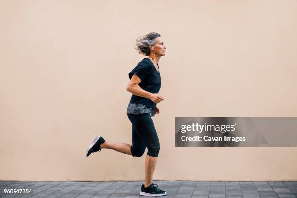 side view of woman jogging on footpath against wall - precalentamiento fotografías e imágenes de stock