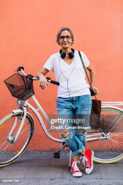 portrait of confident woman with bicycle standing against wall - cavan images stock-fotos und bilder