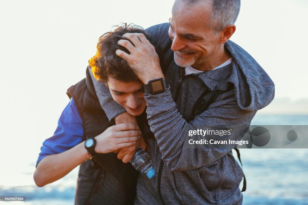 Playful father and son playing while exercising at beach against sky