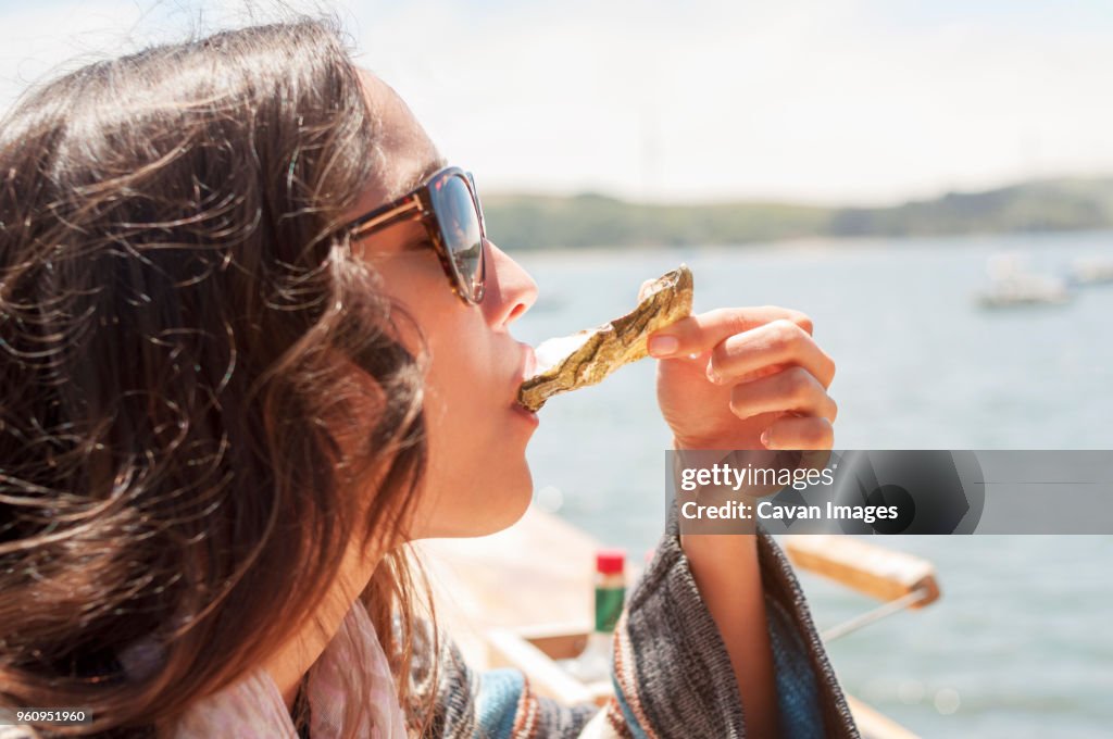 Close-up of woman eating oyster against sea on sunny day