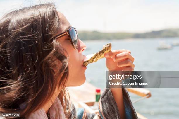 close-up of woman eating oyster against sea on sunny day - oysters stockfoto's en -beelden