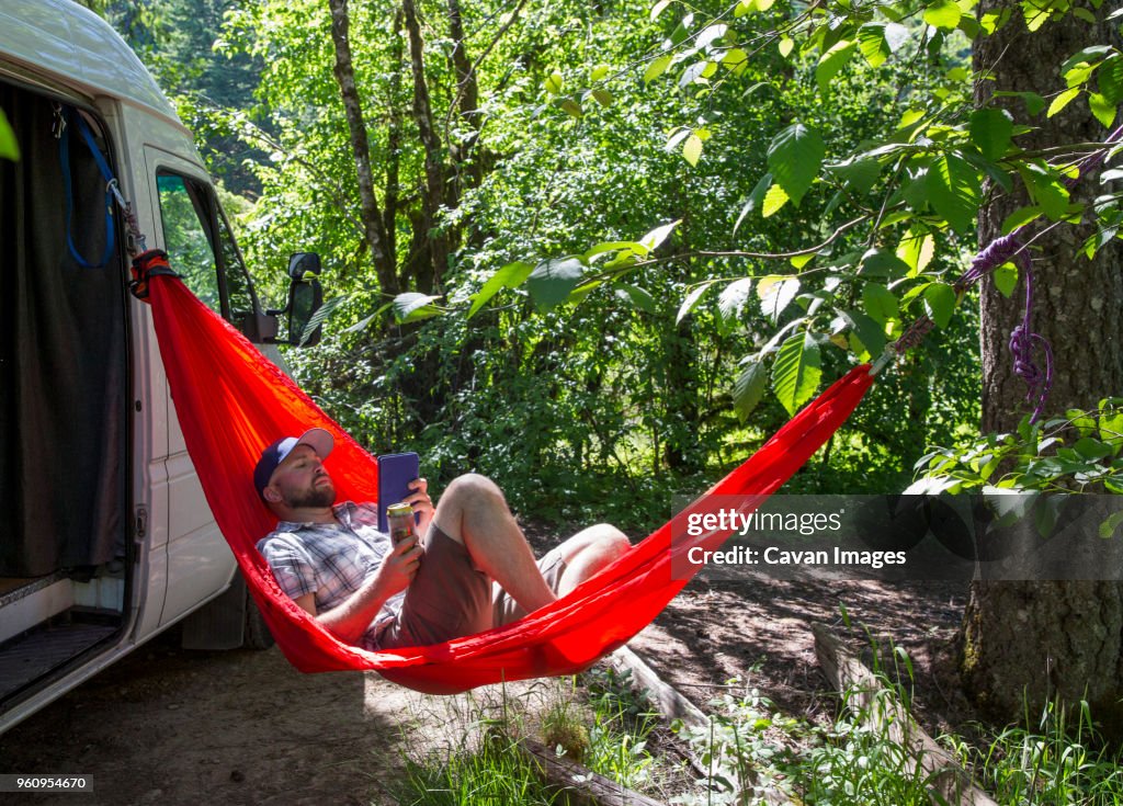 Tourist using tablet computer while resting in hammock against motor home at forest