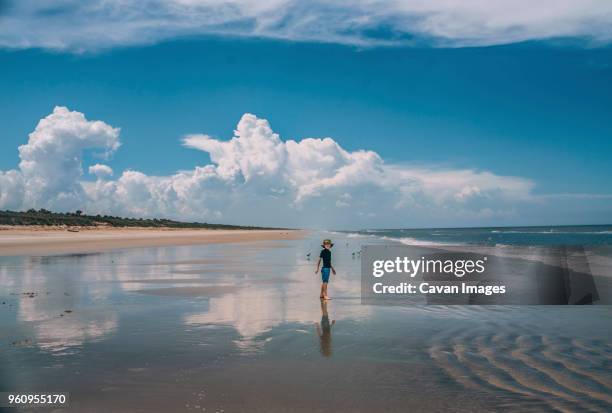 boy standing at new smyrna beach against cloudy sky - ニュースムーナ・ビーチ ストックフォトと画像