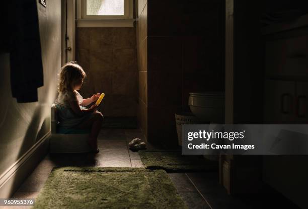 side view of baby girl on potty while holding popsicle in darkroom at home - girls peeing stock pictures, royalty-free photos & images