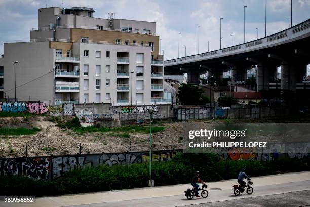 People ride bicycles past a grafitti on May 21, 2018 in Aubervilliers, in the suburbs of the French capital Paris. - French President Emmanuel Macron...