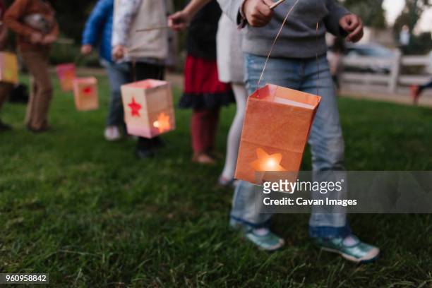 low section of children carrying illuminated paper lanterns while walking on field - lampion stockfoto's en -beelden