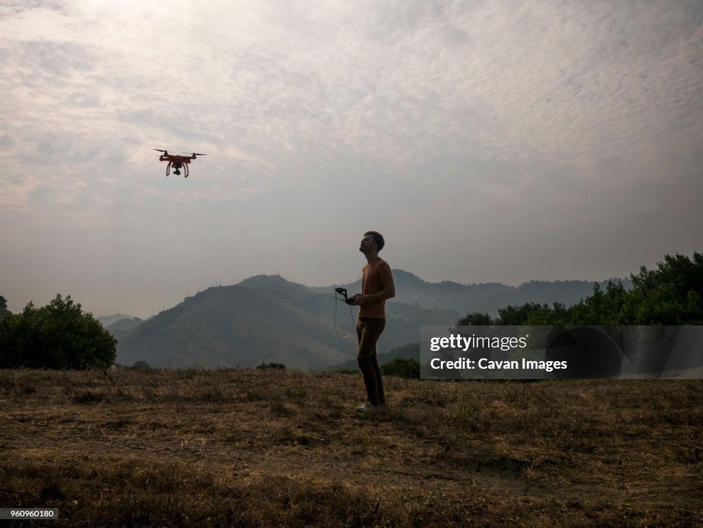 Side view of man operating drone through remote control against mountains