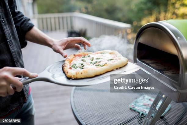 midsection of man examining food on pizza peel by oven at porch - pá de pizza imagens e fotografias de stock