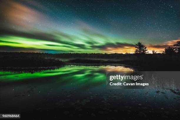 reflection of aurora borealis on calm lake at night - northern lights michigan stock-fotos und bilder