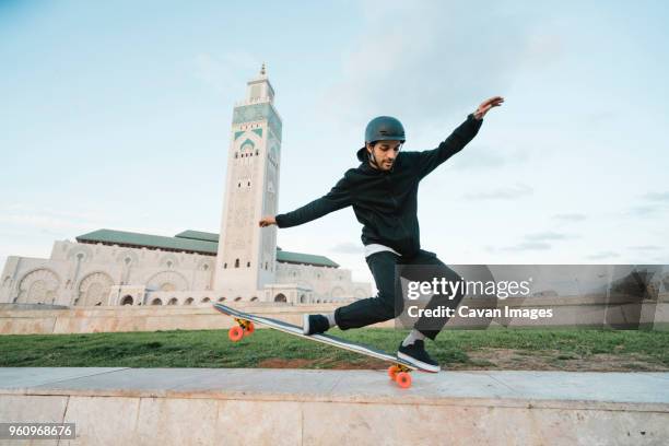 full length of man performing stunt on skateboard against mosque hassan ii - islamic action front stock pictures, royalty-free photos & images