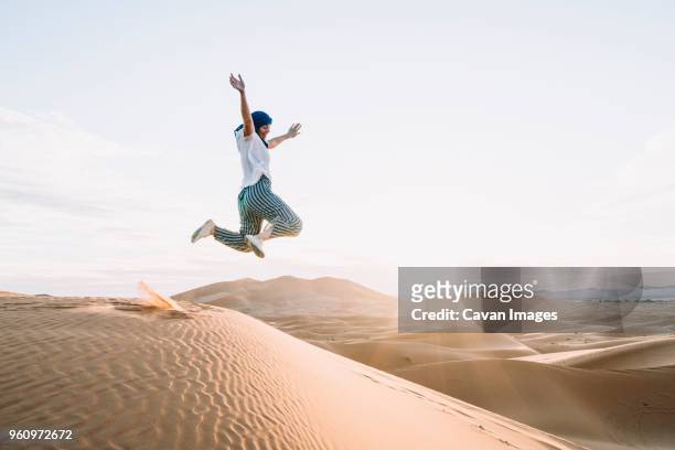 happy woman jumping at merzouga desert against sky - morocco tourist stock pictures, royalty-free photos & images