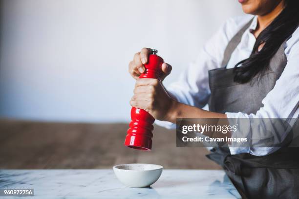 midsection of woman using pepper mill in kitchen - pepper mill stock pictures, royalty-free photos & images