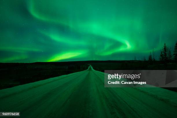 scenic view of aurora borealis over snow covered road - whitehorse stock pictures, royalty-free photos & images