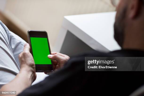 man sat at desk using mobile phone displaying a green screen - sattel bildbanksfoton och bilder