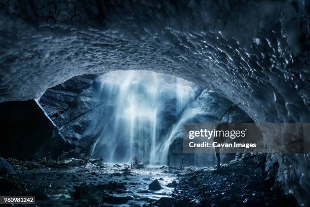 side view of man looking at waterfall while standing in ice cave - ice cave imagens e fotografias de stock