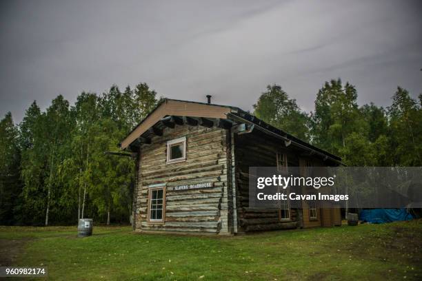 slavens roadhouse on field by trees at yukon_charley rivers national preserve against cloudy sky - houses of alaska stock pictures, royalty-free photos & images