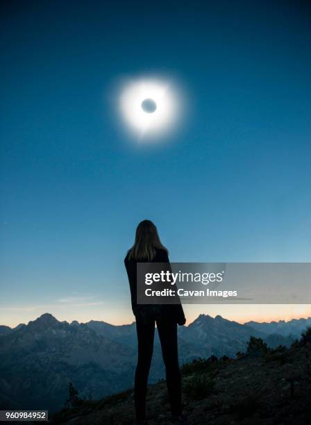 rear view of woman standing on field at sawtooth range during solar eclipse against sky - eclipse fotografías e imágenes de stock