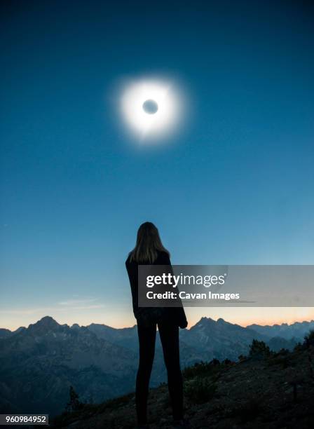 rear view of woman standing on field at sawtooth range during solar eclipse against sky - zonsverduistering stockfoto's en -beelden