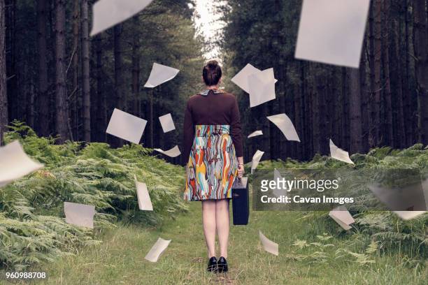 rear view of businesswoman with briefcase standing amidst falling documents at forest - woman filling out paperwork stock-fotos und bilder