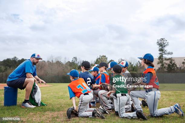 side view of coach talking to baseball team on field - baseball fields stock-fotos und bilder