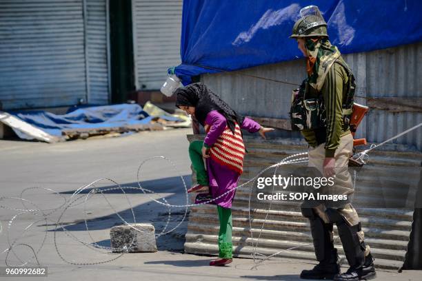 Kashmiri girl tries to cross concertina wire that was erected by the Indian troopers during restrictions imposed ahead of a march to the martyrs...