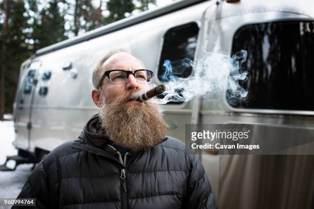 thoughtful mature man smoking cigar outside caravan in forest - arrêt tabac photos et images de collection