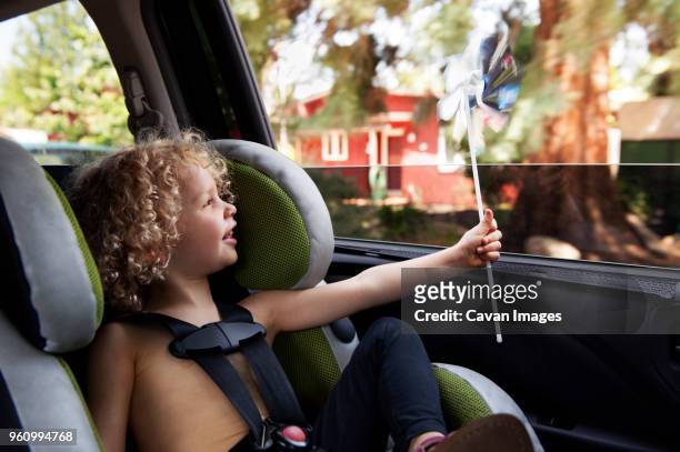 happy girl looking at spinning pinwheel while sitting in carseat - paper windmill stock-fotos und bilder