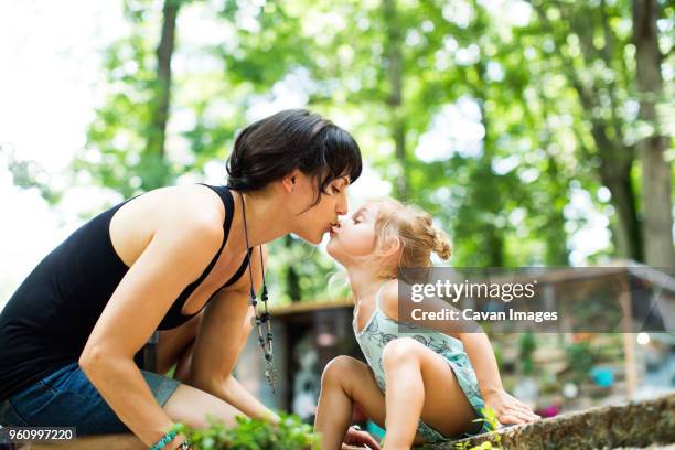 loving daughter kissing mother on mouth while sitting in backyard - kyssa på munnen bildbanksfoton och bilder