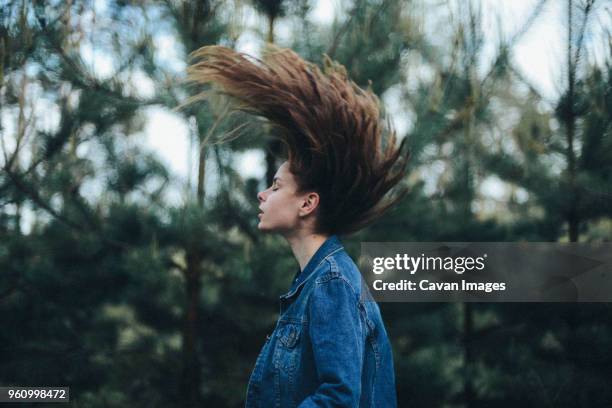 side view of woman tossing hair while standing in forest - hair toss stockfoto's en -beelden