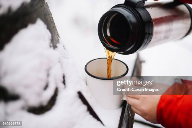 cropped hands of woman pouring black coffee from insulated drink container into mug on snow - insulated drink container foto e immagini stock