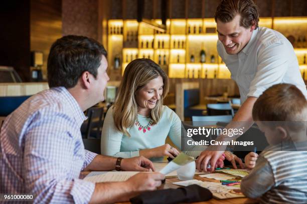 happy waiter assisting family in reading menu at restaurant table - family ordering at restaurant stock pictures, royalty-free photos & images