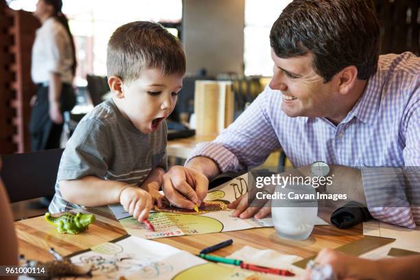 happy father looking at shocked boy while coloring menu in restaurant - children restaurant stockfoto's en -beelden