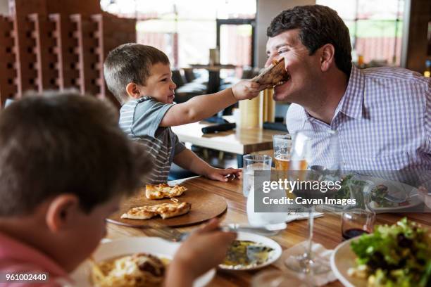 boy feeding pizza to father in restaurant - restaurant kids stockfoto's en -beelden