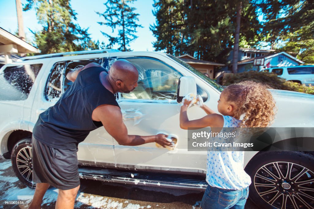 Father and daughter washing car in driveway